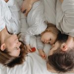 Father, mother, and daughter bonding on a bed, embracing family moments.