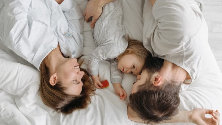 Father, mother, and daughter bonding on a bed, embracing family moments.