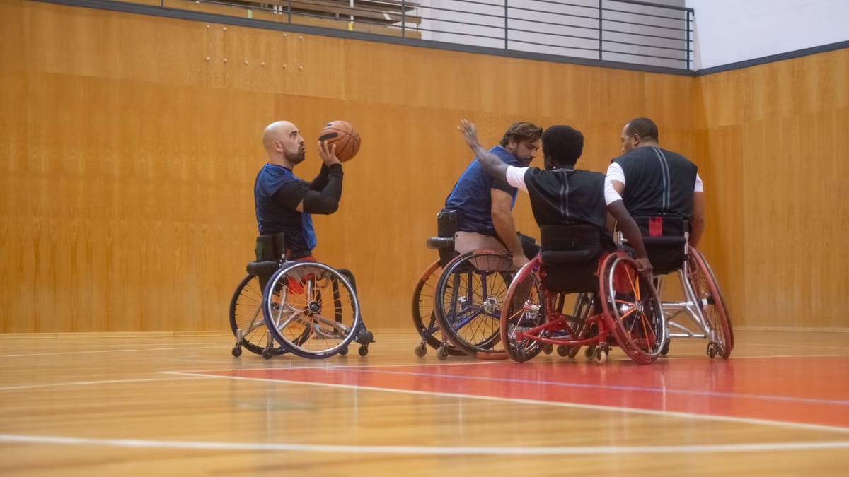 A group of athletes playing wheelchair basketball indoors on a wooden court.