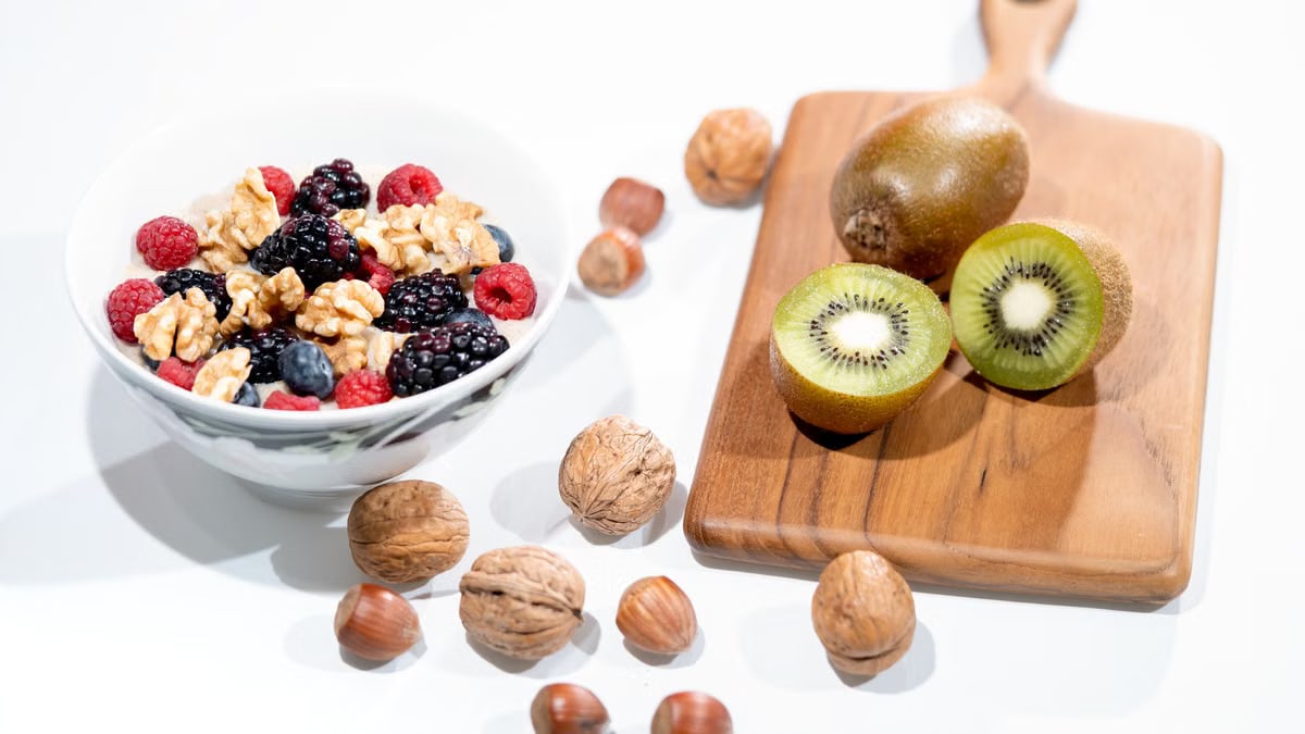 A vibrant bowl of mixed berries, walnuts, and kiwi on a cutting board. Perfect for a healthy breakfast.